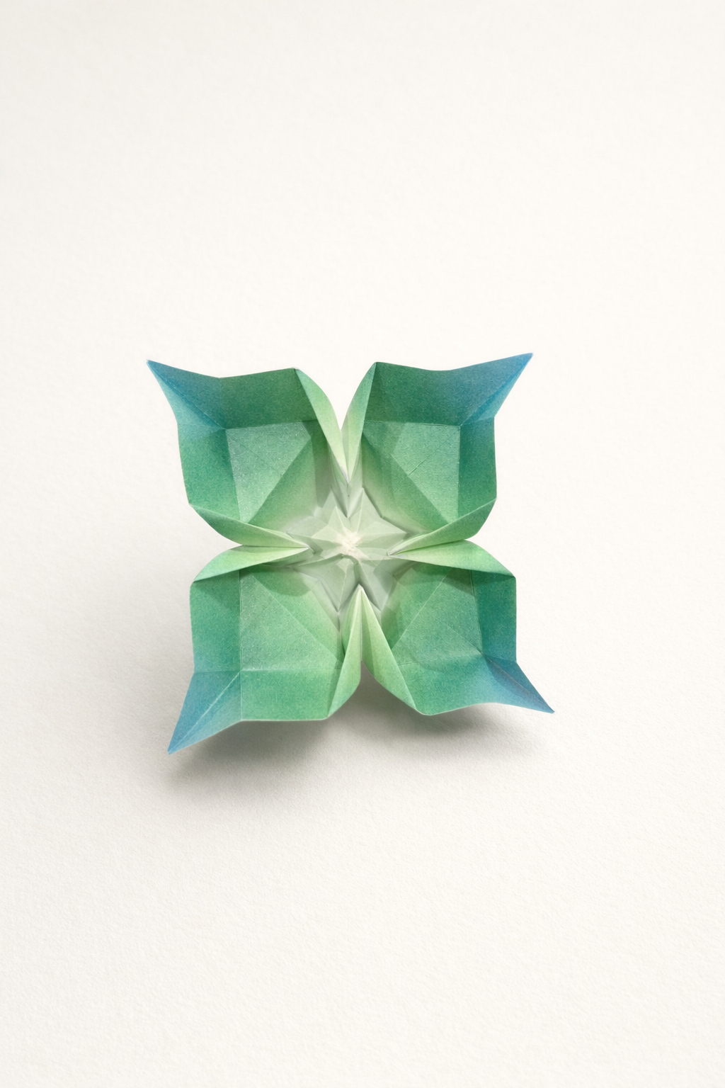 Emergence in Four Directions — single sheet of paper unfolds into a quiet geometry of expansion—four wings, four thresholds, a moment suspended between symmetry and motion. The gradients of green to blue evoke growth at its most fragile stage, like a form just beginning to understand its own structure. At the center, tension gathers and releases, suggesting both a point of origin and a pulse outward—an object that feels less folded than awakened.